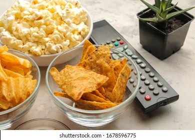 Popcorn And Various Snacks And A Tv Remote Control On A Light Concrete Table. Concept Of Watching A Movie Or Video At Home. 