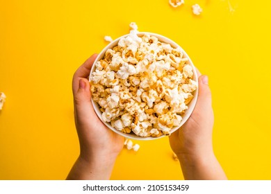 Popcorn viewed from above on yellow background. Child eating pop-corns. Human hand. Cinema snack concept.