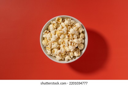 Popcorn In A White Bowl Placed On A Red Background. View From Above.