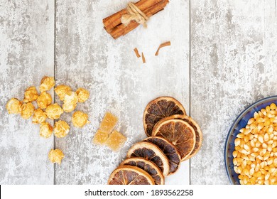 Popped and unpopped corn kernals on a light grey wooden background shot from above, orange slices, cinnamon, apple slices for National Popcorn Day 19 January 2021