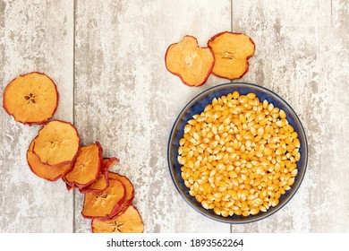 Popped and unpopped corn kernals on a light grey wooden background shot from above, orange slices, cinnamon, apple slices for National Popcorn Day 19 January 2021