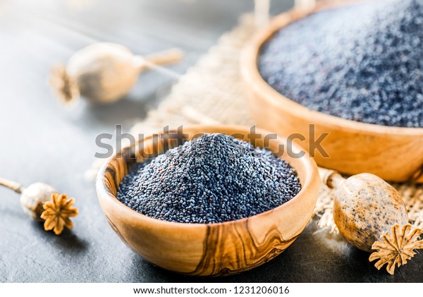 Poppy seeds in small wooden bowl on dark\
table. Poppies head on board with\
backlight.