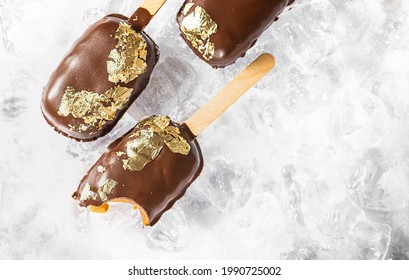 Popsicles, Covered With Chocolate, With A Leaf Of Edible Gold On Top On An Icy Background With Snow. Popsicle And Sweet Dessert On A Stick. Top View