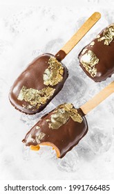 Popsicles, Covered With Chocolate, With A Leaf Of Edible Gold On Top On An Icy Background With Snow. Popsicle And Sweet Dessert On A Stick. Top View