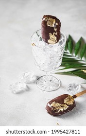 Popsicles, Covered With Chocolate, With A Leaf Of Edible Gold On Top On A Light Concrete Background. Popsicle And Sweet Dessert On A Stick. Selective Focus