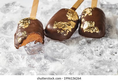 Popsicles, Covered With Chocolate, With A Leaf Of Edible Gold On Top On An Icy Background With Snow. Popsicle And Sweet Dessert On A Stick. Top View