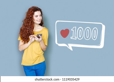 Popular blogger. Cheerful popular blogger looking glad while standing with a smartphone and checking the number of followers - Shutterstock ID 1119035429