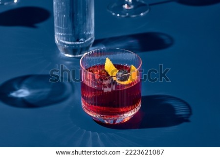 Popular cocktail negroni with gin and vermouth on blue background with shadow. Negroni cocktail on coloured background in trendy style. Contemporary concept with alcohol beverage. Bartender cocktail