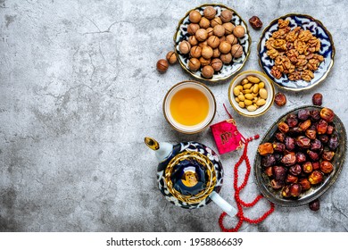 Popular Food During Iftar  - Macadamia Nuts, Pistachios, Walnuts, Dry Dates. Karan, Rosary, Teapot, Bowl With Black Tea On Concrete Background Top View Flat Lay Muslim Holiday Of Holy Month Of Ramadan