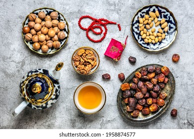 Popular Food During Iftar  - Macadamia Nuts, Pistachios, Walnuts, Dry Dates. Karan, Rosary, Teapot, Bowl With Black Tea On Concrete Background Top View Flat Lay Muslim Holiday Of Holy Month Of Ramadan