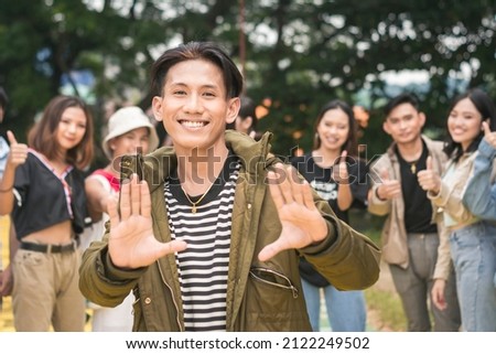 A popular guy posing in front of his friends in the background. An admired man with his supporters. Outdoor scene.