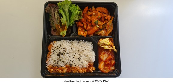 Popular Korea food bento with Dakgalbi, Spicy Chicken Stir Fry chicken with savoury rice, fresh salad and shreded egg with kim chi in take away packing.