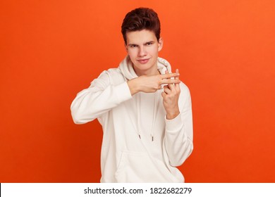 Popular male blogger in casual style sweatshirt with hood showing hashtag sign with fingers, recommending popular websites. Indoor studio shot isolated on orange background
