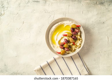 Popular middle eastern appetizer labneh or labaneh, soft white goat milk cheese with olive oil, hyssop or zaatar, served with pita bread over grey table, flaylay.