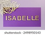 Popular and modern baby girl fashion name ISABELLE in wooden English language capital letters spilling from a pile of letters on a purple background framed