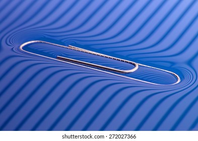 Popular Physics: Surface Tension, Paperclip On Blue Water Surface, Lighted Through Stripes