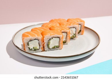 Popular sushi roll - philadelphia with salmon and cream cheese. Philadelphia maki in ceramic plate on coloured backdrop. Sushi menu concept. Modern japanesse food. Maki sushi in minimal style.