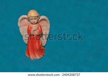 Porcelain angel in red clothes on a blue background with pink wings.                              