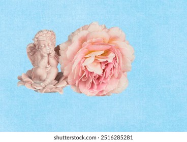 Porcelain angel, with wings, smiling, on a blue background, sitting near a large rose flower, for a postcard, for congratulations. - Powered by Shutterstock