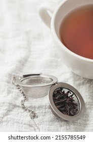 Porcelain Cup With Hot Black Tea And Infuser With Loose Tea On White Kitchen Towel