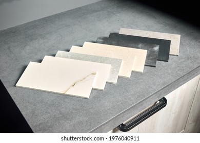 Porcelain stoneware square samples laid on kitchen countertop as examples of future kitchen fasade exterior. Porcelain stoneware exhibitor for finishing of kitchen, cabinets countertops and surfaces.
