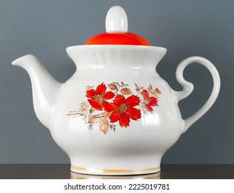 Porcelain teapot on a grey background. A teapot with a red floral pattern.