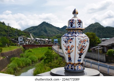 A porcelain vase decorated in traditional japanese Imari style - red, blue and gold colors, scenic landscape of Arita town in the background - Shutterstock ID 2246772089