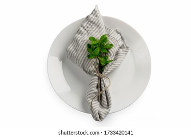 Porcelain white plate with laying folded striped napkin and rustic rough rope and ribbon on isolated background with green plant mint or basil branch decoration  - Powered by Shutterstock