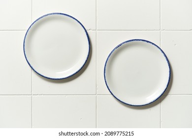 Porcelain White Saucer With Blue Edge On A White Tile Table. Flat Lay View Of Empty Plate.