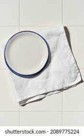 Porcelain White Saucer With Blue Edge On A White Tile Table. Flat Lay View Of Empty Plate.