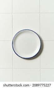 Porcelain White Saucer With Blue Edge On A White Tile Table. Flat Lay View Of Empty Plate.