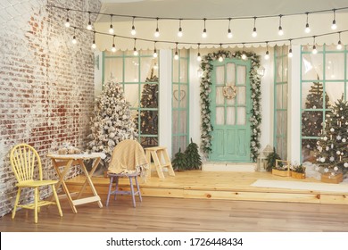 Porch of house with Christmas decorations. Retro street garland with light bulbs over the terrace of house. Garden table and chairs on the winter terrace background of Christmas trees - Powered by Shutterstock