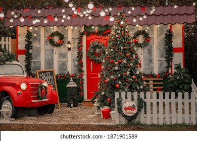 The Porch Of The House Is Decorated For Christmas. Street Christmas Decor With Artificial Snow And Red Car Next To Christmas Veranda Decorations