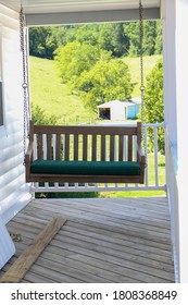 A Porch Swing Has A View Of The Hilly Farm Behind.