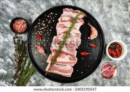 Pork belly with spices and aromatic herbs on a black plate, top view