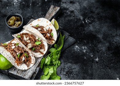 Pork carnitas tacos on corn tortillas with onion and lime. Black background. Top view. Copy space.