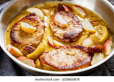 pork chops in apple cider cream sauce with caramelized sliced apples in a pan on a wooden table, horizontal view from above, close-up