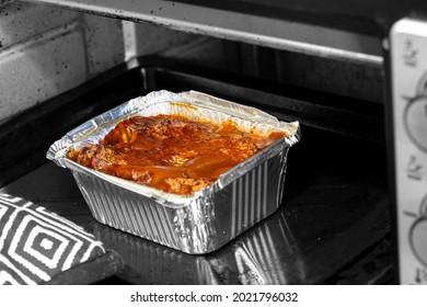 Pork faggots with onion gravy, in a foil container, cooked in an electric oven. Selective colour image