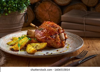 Pork Knuckle With Baked Potatoes On Rustic Kitchen Table At Dark Wooden Background, Front View. Pork Leg Done, German Food