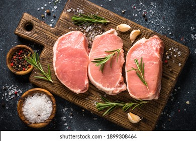 Pork meat. Fresh pork steaks on cutting board with ingredients for cooking. Top view at black stone table. - Powered by Shutterstock