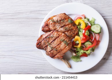 Pork meat grilled with fresh vegetable salad on a white plate. a top view of a horizontal 