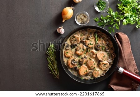 Pork medallions in mushroom gravy in cast iron pan over dark stone background with copy space. Top view, flat lay