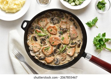 Pork medallions with mushroom sauce in cast iron pan over white stone background. Top view, flat lay