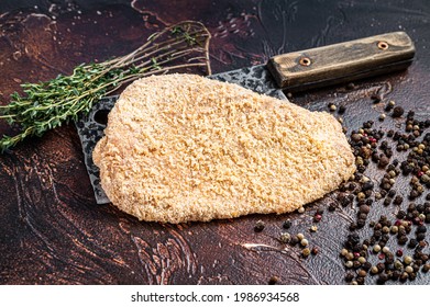 Pork Raw Escalope or schnitzel on a meat cleaver with herbs. Dark background. Top view