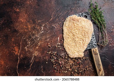 Pork Raw Escalope or schnitzel on a meat cleaver with herbs. Dark background. Top view. Copy space.