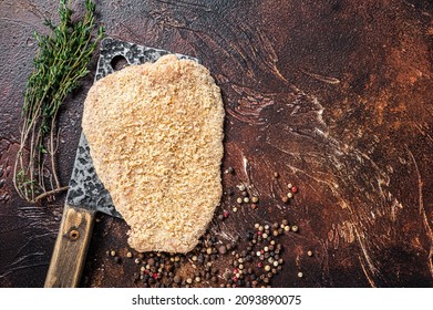 Pork Raw Escalope or schnitzel on a meat cleaver with herbs. Dark background. Top view. Copy space
