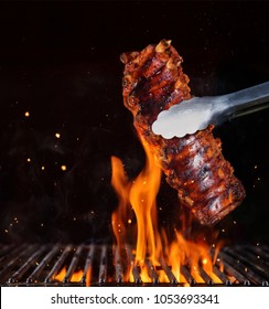 Pork ribs over flaming grill grid, isolated on black background. Barbecue and cooking