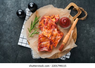 Pork ribs. Raw meat. Raw pork ribs in marinade with spices, rosemary, tomato sauce and garlic on old wooden stand on black stone table background. Barbecue concept. Top view. Mock up. - Powered by Shutterstock