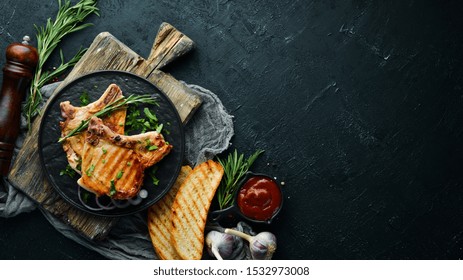 Pork Steak On A Bone With Rosemary And Greens In A Black Plate. Top View. Free Copy Space.