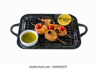 Pork Tenderloin Wrapped In Bacon And Oven Baked With Cheese. The Meat Is Put On Wooden Skewers. On Top Are Cherry Tomatoes And Olives. Nearby Is A White Bowl With Olive Sauce, A Slice Of Lemon And A S